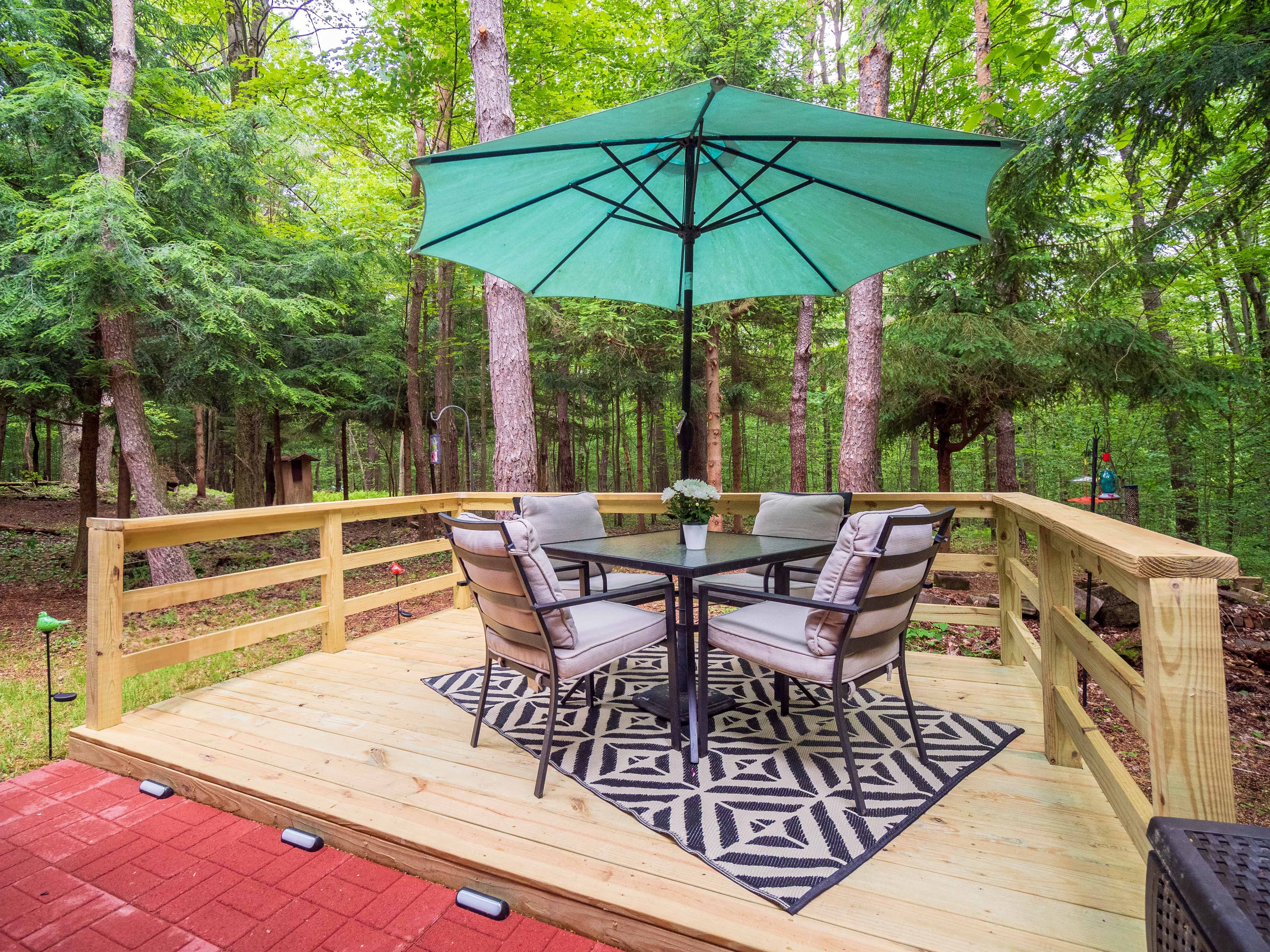 The back deck with a table and green umbrella, surrounded by summer woods